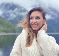 a woman wearing a white sweater in front of a lake